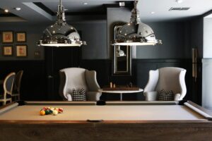 Billiard tafel met twee grijze stoelen en zilver hangende lampen boven de tafel.